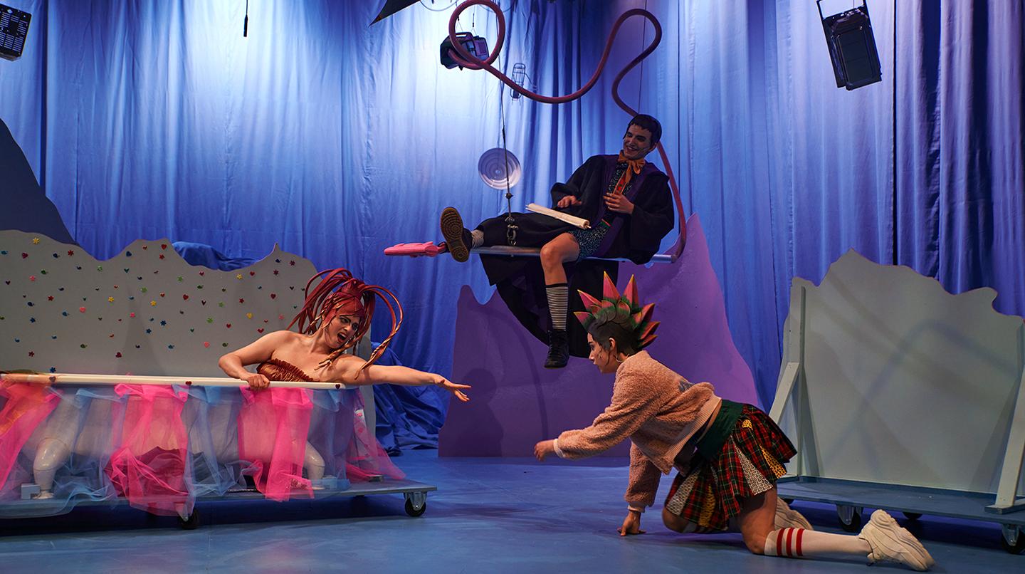 En scen där en mimskådespelare sitter i ett badkar, en annan hänger från en stol från taket och en tredje kryper på alla fyra på golvet. Från föreställningen Det förlovade landet, från scenkonstprojektet SKH möter unga, 2021.