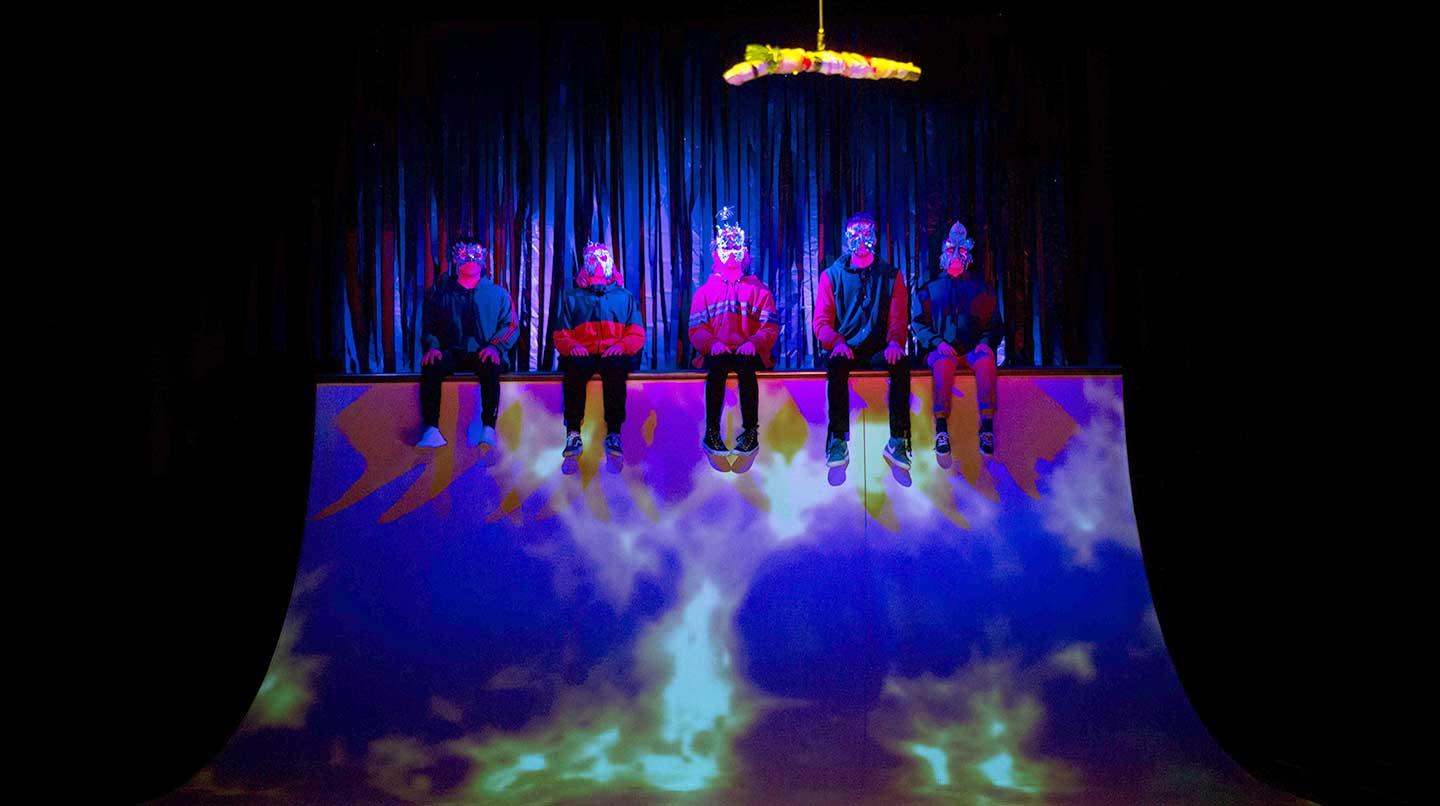Fem skådespelare med ytterkläder, sitter uppe på en hög ramp på en scen. Från Unga StDH-föreställningen Fem fåglar, 2018.