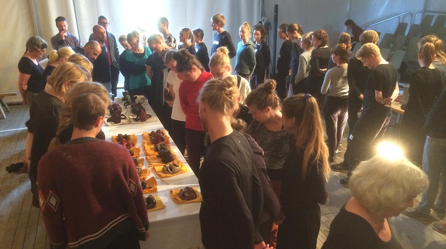 Folksamling runt ett bord uppdukat med olika teatermasker. Från Nomadskolan på Fårö, ett internationellt studentprojekt från 2015.