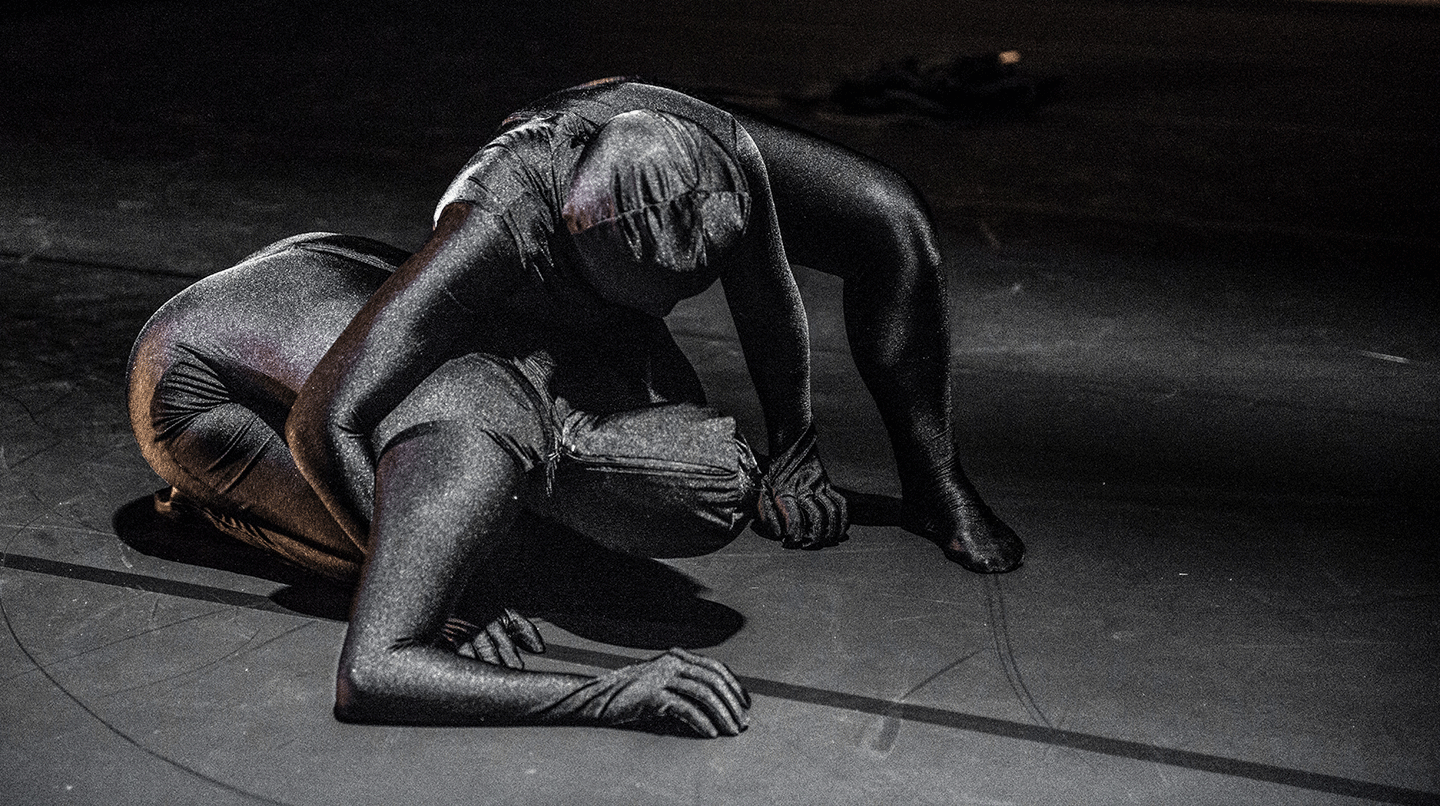 Två dansare i rörelse på golvet, iklädda svartglittriga heldräkter. Från dansföreställningen Manifesto, 2013.