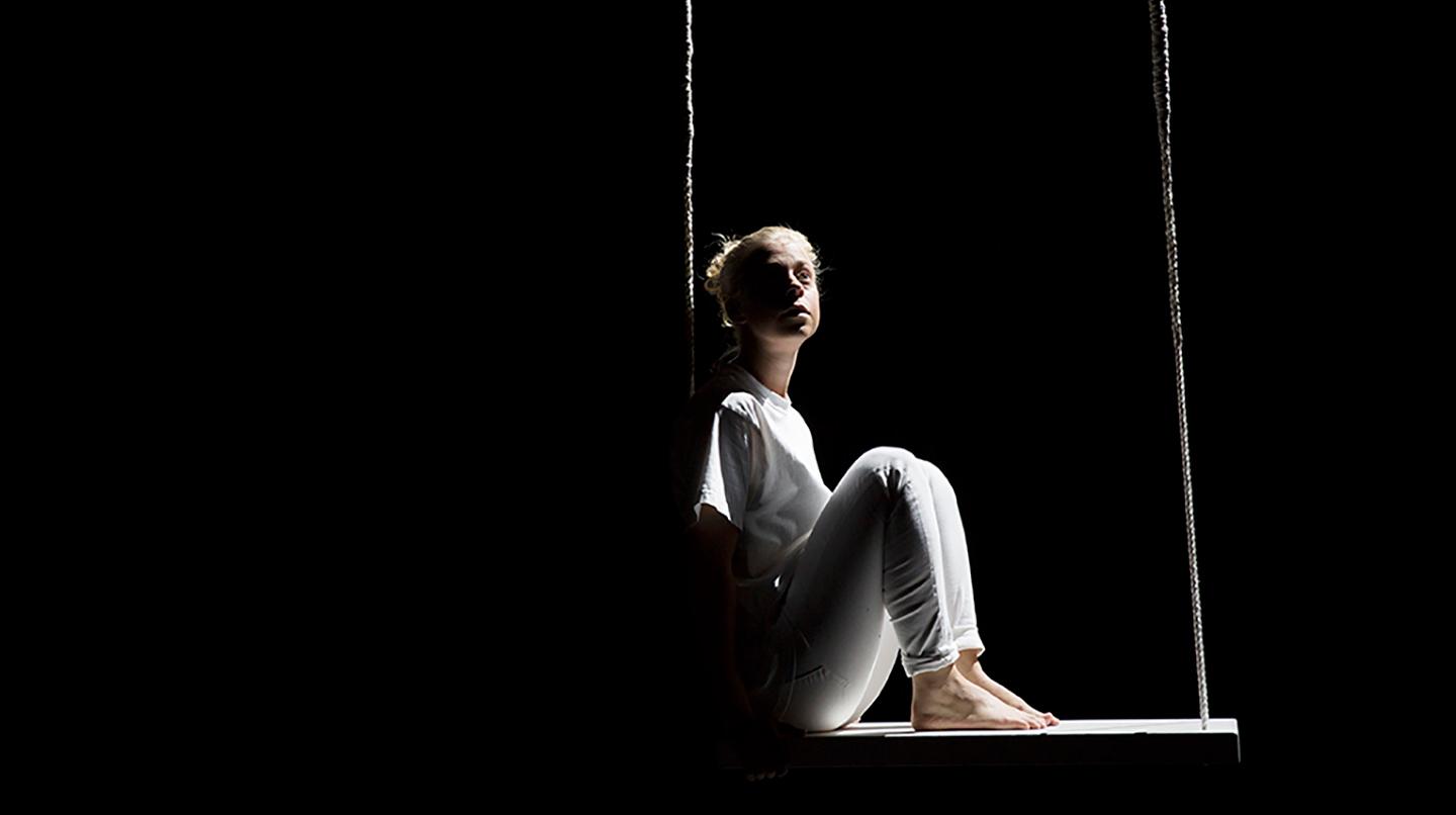 En mimskådespelarstudent sitter i en gunga på scenen. Från en Departureföreställning 2016.