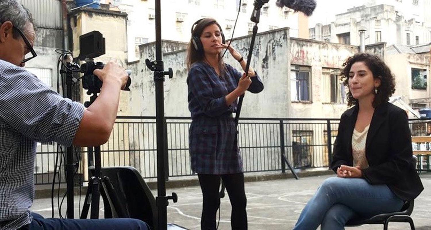 Ett filmteam filmar en kvinna som sitter på en stol på ett tak. Från ett internationaliseringsprojekt.