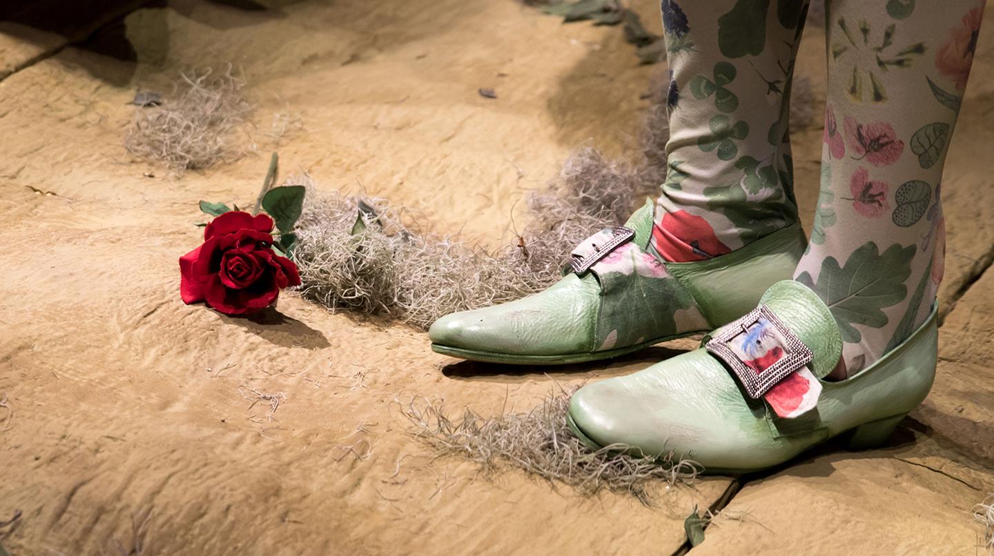 Närbild på ett par fötter i gröna skor plus en ros liggande intill.