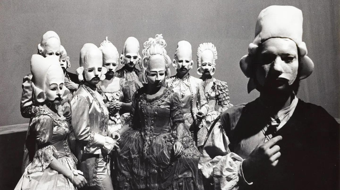 Ett tiotal skådespelare med teatermasker och peruker, iklädda historiska teaterkläder, tittar in i kameran. Statens musikdramatiska skola ger Glücks "Orfeus och Eurydike" i regi av Etienne Glaser, 1970. 