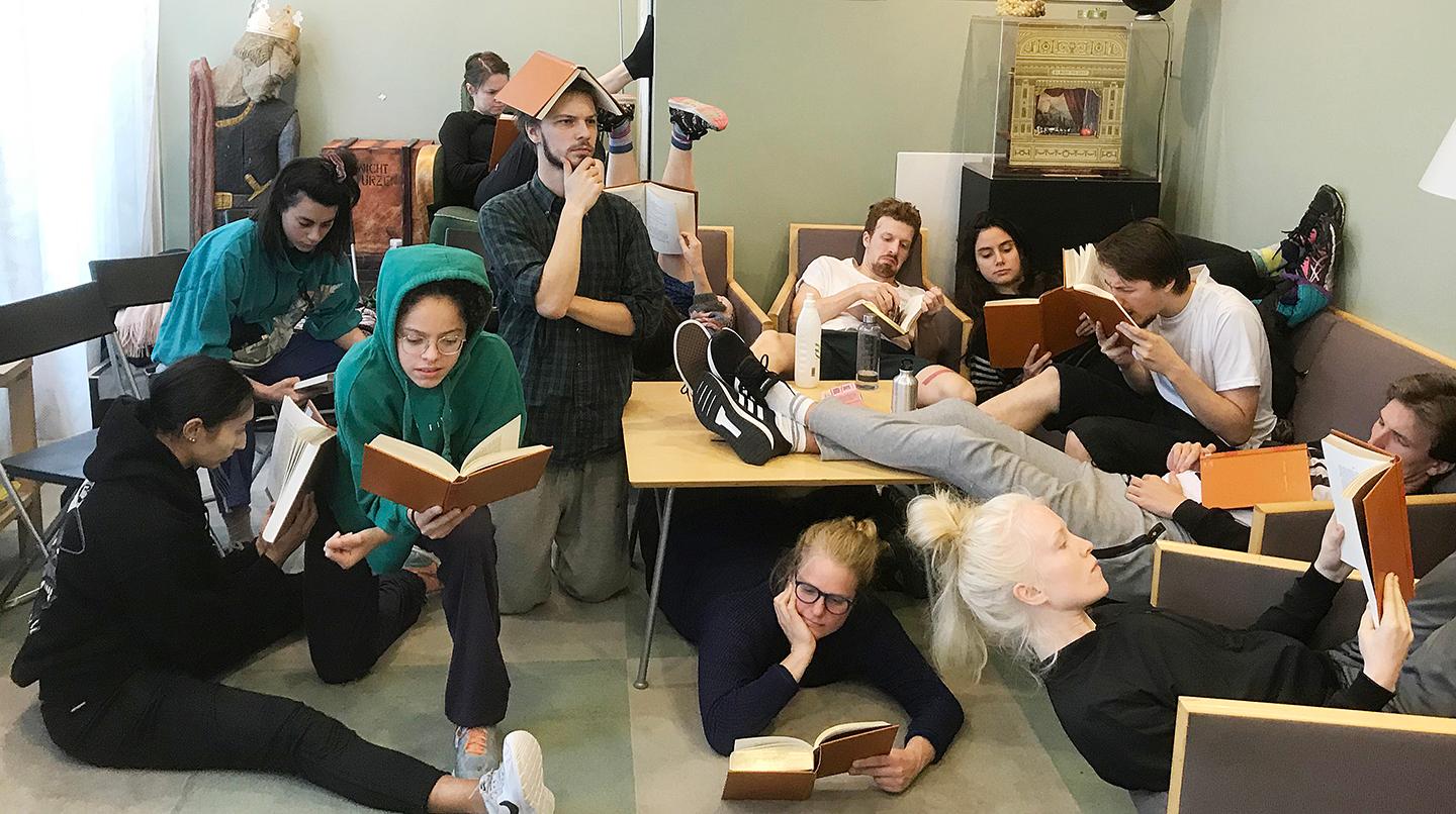 Kandidatstudenter från mimskådespeleri 2022 ligger huller och buller i biblioteket med varsina böcker i handen och läser.