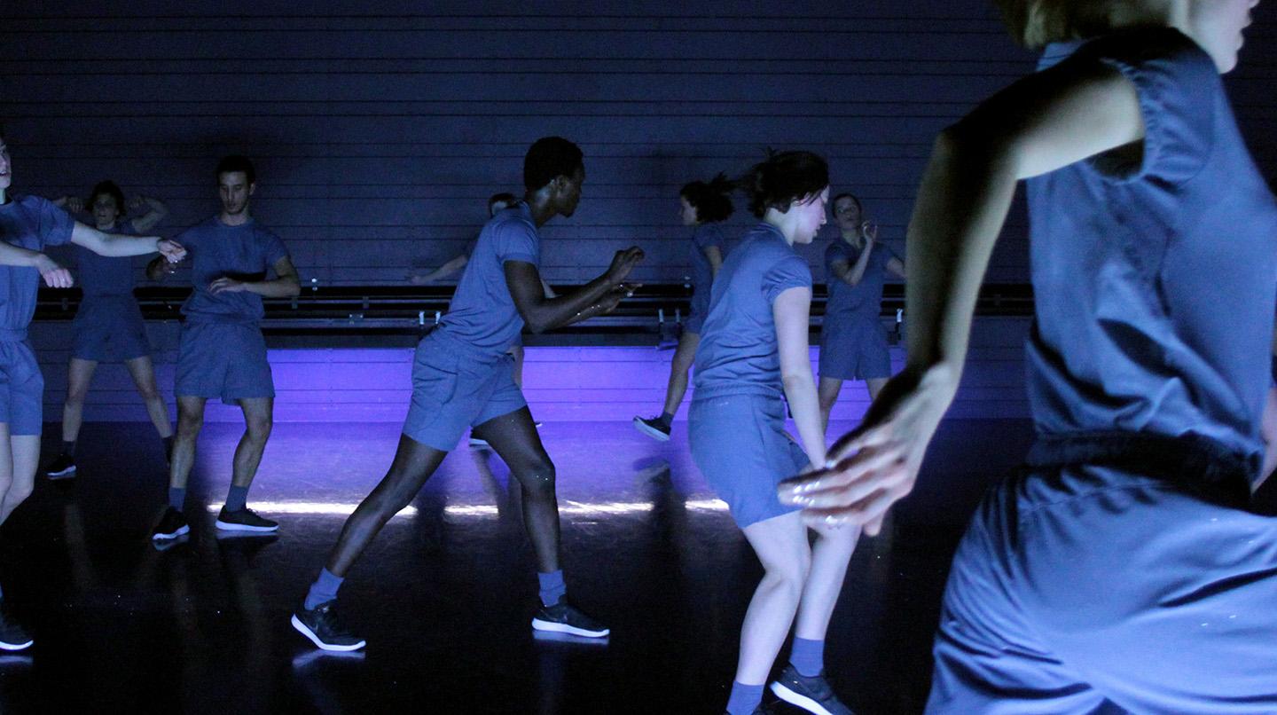 Blåklädda dansare springer runt på en scen, i examensföreställningen Splendour, 2018.