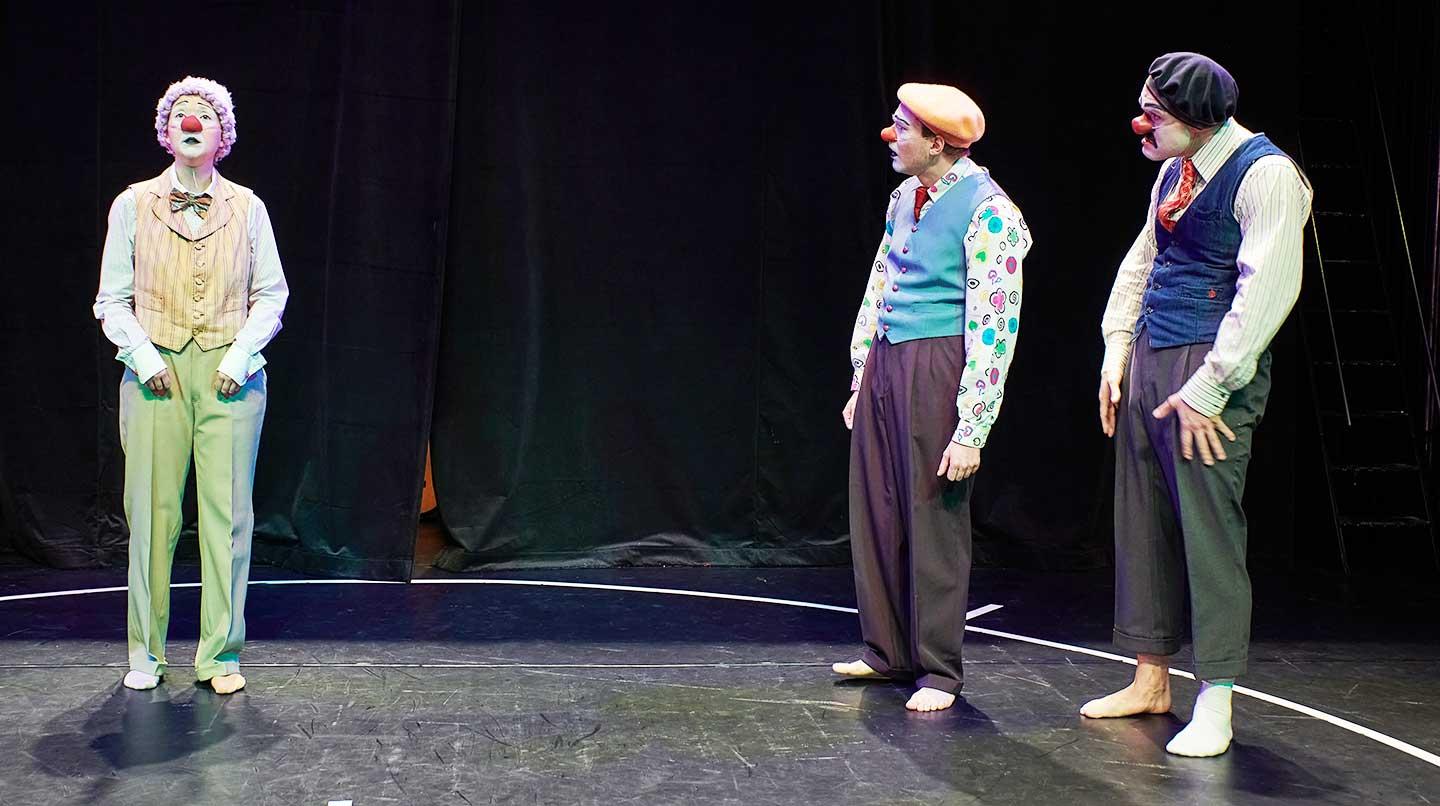 Tre clowner står på en scen. Två står vid sidan om och tittar mot den tredje.