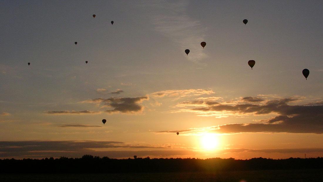 Ett tiotal luftballonger i silhuett mot solnedgången.